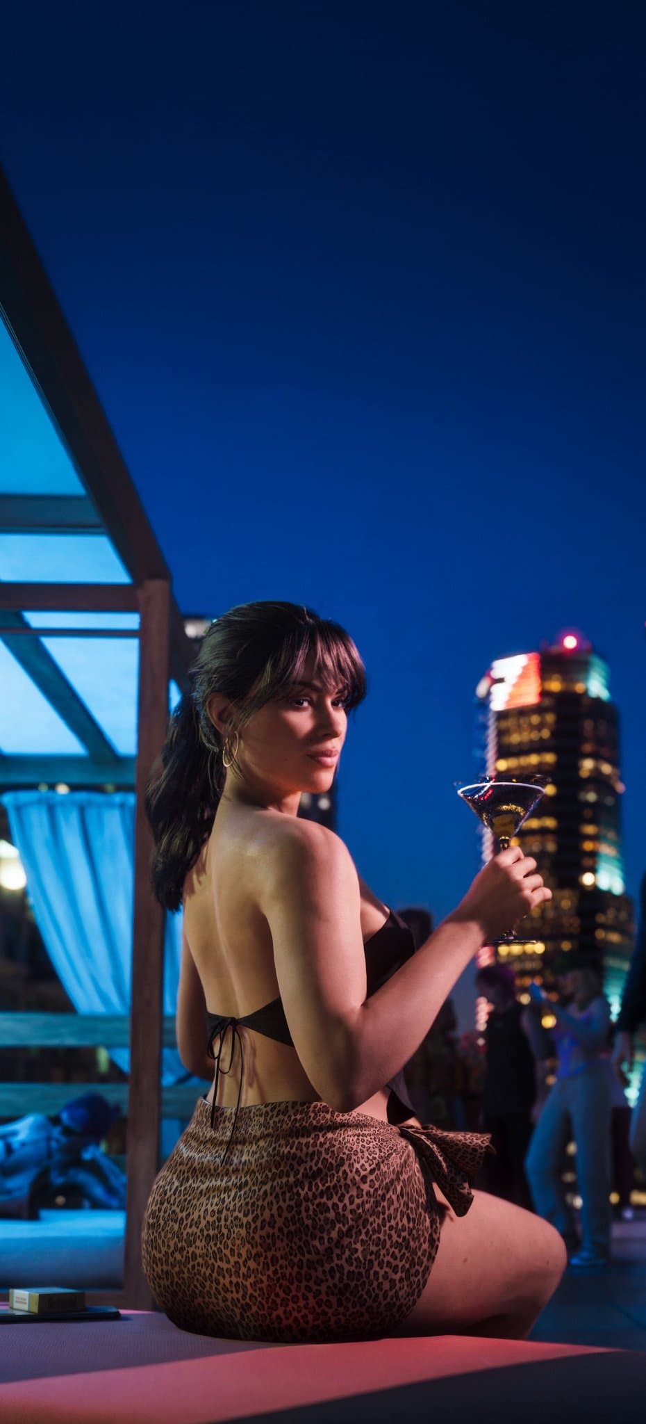 Vertical GTA VI phone wallpaper showing Lucia Caminos holding a cocktail at a nighttime Vice City rooftop venue.